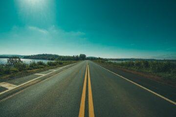 panoramic photography of road between grasses and body of waters