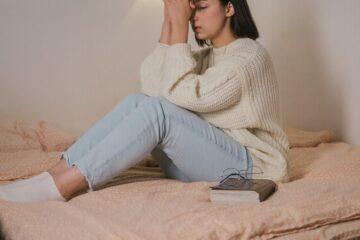 woman in white sweater and blue denim jeans praying on bed