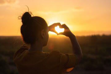 woman sitting while showing heart sign hands