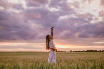 woman in white dress standing in field with raised hand