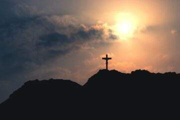 silhouette of cross on mountain under cloudy sky during sunset