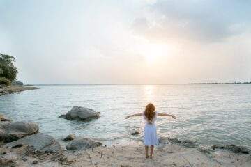 woman in white shirt standing on gray rock near body of water