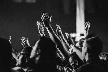 grayscale photo of people raising their hands